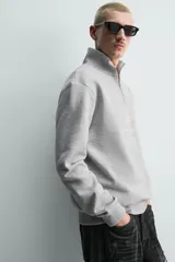Sudadera de corte regular con cuello subido y cierre frontal de cremallera. Presenta mangas largas, puños y ruedo en rib, y bordados decorativos a contraste en el frente.