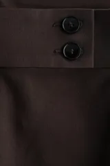 Pantalón de sarga color marrón oscuro, de tiro alto y corte bootcut. Cuenta con pretina ancha con detalle de dos botones en el lateral, pliegues marcados en el frente y bolsillos laterales.