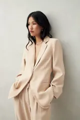 Blazer color beige con finas rayas verticales, de corte entallado, solapas clásicas y cierre con un botón.