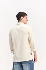 Camisa de manga larga color beige, de tejido texturado con cierre frontal de botones y cuello camisero clásico.