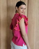 Musculosa de tejido de punto color fucsia con detalles de costuras en color naranja en el cuello, ruedo y volados de las mangas.