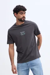 Remera gris oscuro de algodón, con corte regular fit, cuello redondo y mangas cortas. Presenta un pequeño estampado tipográfico en el pecho con letras celestes.