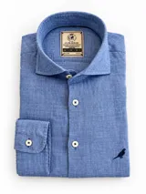 Camisa slim fit de lino color azul, con cuello italiano, mangas largas, botones frontales claros y bordado de un ave en la parte inferior.