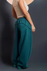 Pantalón de estilo deportivo en color verde petróleo, con cintura elástica y diseño de corte ancho. Presenta costuras decorativas y bolsillos traseros.