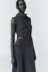Vestido midi de tejido texturizado en color gris oscuro, con cuello alto fluido, diseño sin mangas y acabados deshilachados. Incluye un cinturón fino de cuero en color marrón con hebilla metálica y cierre de cremallera oculta en la espalda.