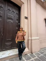 Camisa de color marrón chocolate con cuello redondo grande y ribetes en color amarillo vibrante. Presenta cierre frontal con botones amarillos, mangas largas con puños elásticos y un corte holgado.