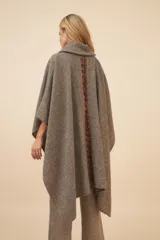 Poncho de lana color beige con cuello alto, bolsillos frontales y detalle de cordones de cuero en los bordes de los bolsillos.