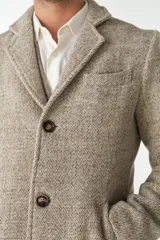 Abrigo masculino de lana color beige, con cuello con solapa, manga larga y forro interior. Tiene bolsillos laterales y cierre frontal con botones.