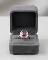 Anillo de plata con piedra central rectangular de rubí en corte esmeralda, rodeada por un pavé de circonias cúbicas y detalles en los laterales.