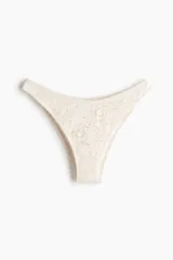 Vedetina cheeky de baño color crudo, con textura de encaje floral y tiro bajo.