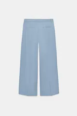 Pantalón wide leg de tiro medio confeccionado en hilatura de algodón, color beige, con trabillas en la cintura, bolsillos laterales ocultos y detalle de pliegues en el delantero. Cierre frontal con cremallera, botón y ganchos metálicos.