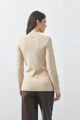 Polera de tejido de punto color beige, con cuello alto, manga larga y detalle de lazo ajustable en la cintura que aporta estructura a la silueta.