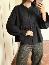 Camisa negra de corte peplum con detalles de bordado inglés en el pecho, cuello redondo y mangas largas con puños acampanados.