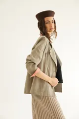 Chaqueta corta de inspiración motoquera color beige, confeccionada en lino fantasía, sin forro, con cierres decorativos, broches de presión y bolsillos delanteros funcionales. Presenta detalle bajo el cuello y en vueltas de mangas en color mostaza y rayas.
