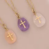 Collar con cadena dorada y dije de piedra natural pulida con cruz dorada incrustada. Disponible en tres colores: rosa, lila y blanco.
