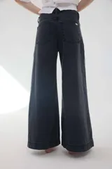 Pantalón jean gris oscuro de tiro medio y piernas anchas, con diseño de cinco bolsillos y cierre frontal con botón y cremallera.