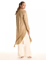 Túnica satinada color dorado con estampado animal print, de silueta oversize y fluida, largo maxi. Cuello a la base con abertura central y botones a tono. Manga larga de corte recto con puños amplios y cierre de botones. Espalda con canesú horizontal recto del cual nace un tablón central profundo. Bajo asimétrico redondeado con tajos laterales profundos, el largo de espalda mayor al largo delantero.