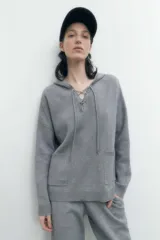 Sweater gris melange de tejido de punto, con capucha y cordones cruzados en el escote.