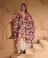 Kaftan largo de corte holgado con estampado abstracto en tonos bordó sobre fondo claro. Presenta escote en V profundo, mangas anchas tipo kimono y un cordón trenzado ajustable en la cintura con terminaciones de borlas.