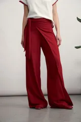 Pantalón de corte amplio y tiro alto, confeccionado en tela con textura tipo lino. Presenta un diseño envolvente en la cintura con un lazo lateral para anudar, creando un efecto de superposición frontal.