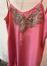 Vestido corto rosado con breteles finos, escote en V con aplique bordado dorado y volados en el ruedo.