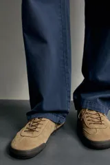 Zapatilla deportiva barefoot de hombre, confeccionada en piel con acabado serraje de color marrón, puntera redondeada, suela fina de goma oscura y detalles en cuero liso en el talón.