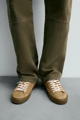 Zapatilla de cordones confeccionada en piel con acabado de serraje. Presenta un diseño liso con detalle en color a contraste en la pieza del talón y suela plana de goma a contraste.