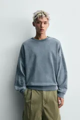 Sudadera de corte relaxed fit confeccionada en tejido de algodón con interior de rizo. Presenta cuello redondo, manga larga y acabados en rib, con un acabado de efecto lavado que le otorga una apariencia única.