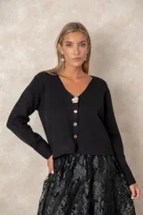 Cardigan de punto fino color negro con escote en V, manga larga y cierre frontal con botones dorados labrados, destacando un botón joya superior en forma de flor.