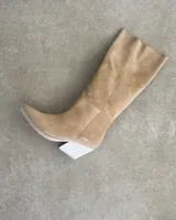 Bota alta de gamuza color beige con punta fina y taco geométrico de madera clara.