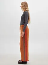 Pantalón ancho y suelto de tejido tipo terciopelo color naranja, con cintura elástica y cordón ajustable. Presenta detalles de pespuntes decorativos a los lados.