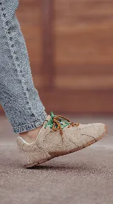 Zapatilla de cuero color beige claro, confeccionada con silueta liviana y diseño urbano. Cuenta con cordones intercambiables bicolores en verde y marrón, y suela de goma flexible.