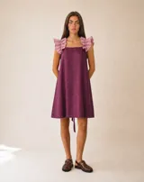 Vestido corto de silueta amplia y evasé, color bordó, con escote cuadrado y volados rosados en los breteles. Cuenta con espalda abierta y lazos regulables.