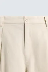 Pantalón relaxed fit color beige confeccionado en tejido de algodón con tacto suave, cintura con pliegues delanteros y cierre frontal con cremallera y botón.