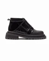 Botineta de estilo urbano con suela track, confeccionada en una combinación de cuero liso y cuero con textura de reptil. Presenta un cierre de solapa con velcro en el empeine y una lengüeta trasera para facilitar el calce.