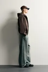 Cazadora de denim de algodón color negro con efecto lavado, de corte relaxed fit, manga larga y capucha. Cuenta con cierre frontal de cremallera, bolsillos frontales tipo canguro y acabados con elástico en puños y cintura.