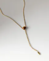 Collar tipo gargantilla en plata de ley con baño de oro de 18k, diseño tipo lazada con una piedra central de ojo de tigre y un colgante en forma de barra fina en el extremo inferior.