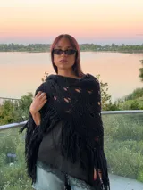 Ruana tejida artesanalmente en lana merino, de color negro, con diseño calado y terminación de flecos largos en los bordes.
