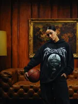 Hoodie negro de corte amplio con estampa frontal de Dennis Rodman y tipografía estilo metal en la parte superior. Cuenta con capucha con cordones ajustables y bolsillo tipo canguro.