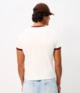 Remera estilo baby tee de color blanco crudo, con cuello redondo y ribetes en contraste de tono bordó. Presenta mangas cortas y una estampa frontal con la inscripción "Worldwide Rhythm".