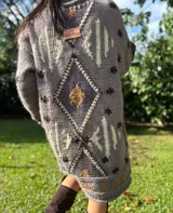 Vestido tipo sweater oversize de lana, tejido a mano con técnica de intarsia y detalles bordados. Presenta un diseño geométrico de rombos en tonos azul marino, beige y verde, con cuello redondo y mangas largas.
