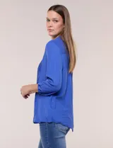 Blusa celeste de silueta suelta y textura liviana, con escote en V, cuello mao y cierre frontal de botones. Cuenta con alforzas verticales en el pecho y mangas tres cuartos con puños elastizados y detalle de galón calado.