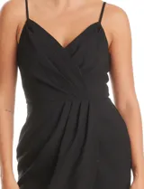 Vestido corto de crepe color negro con escote en V cruzado y drapeado en el busto. Presenta una falda envolvente con diseño drapeado y abertura asimétrica en el bajo, con cierre invisible en la espalda y forro interno.