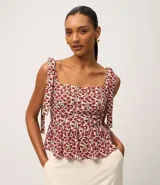 Blusa de viscosa y lino con estampado floral en tonos rojos y blancos. Presenta escote cuadrado, cuerpo ajustado con fruncido en la cintura y bajo con volado (peplum). Los breteles son anchos y se atan con lazos en los hombros.