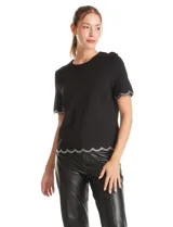 Blusa negra de crepe con cuello redondo y mangas cortas. Presenta terminaciones onduladas en mangas y ruedo, decoradas con una cinta de strass brillante. Cuenta con cierre invisible en la espalda.