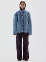 Campera de pelo sintético en color azul, con cuello alto y cierre frontal de botones. Presenta detalles de terminación en cuero vegano color bordó en los bordes, costuras y solapas.