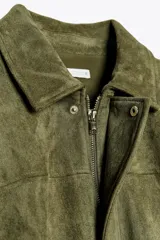 Chaqueta de efecto ante color marrón claro, con cuello solapa, manga larga con trabillas en los hombros y bajo abullonado. Cierre frontal con cremallera y botones ocultos por solapa.