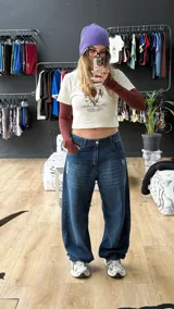 Pantalón de jean azul oscuro de corte wide leg, con diseño holgado y tiro medio. Presenta un pequeño bordado con alas en el bolsillo delantero.