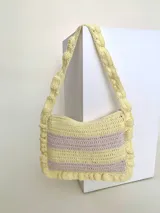 Cartera tipo shoulder bag tejida a crochet en hilo de algodón, con diseño a rayas en tonos de rojo y rosado, y detalles de volados en los bordes y la manija de hombro.