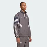 Chaqueta deportiva Adidas del Real Madrid en color gris, con diseño de bloques en blanco y azul marino, cuello alto, cierre frontal y las icónicas tres tiras en las mangas.